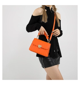 Detailed view of an orange textured leather crossbody bag with a gold heart-shaped buckle