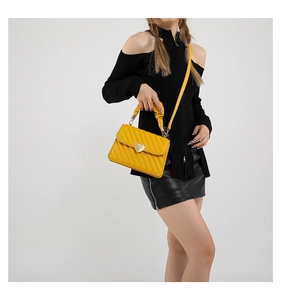 Detail of yellow quilted crossbody bag featuring a golden heart buckle on a model