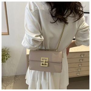 Detail of a chic beige crossbody bag featuring a golden geometric clasp and chain strap