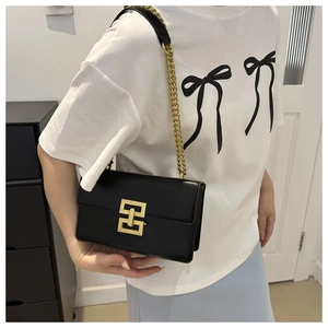 Model wearing a black leather square bag with gold chain strap and geometric clasp