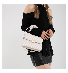 Detail of cream crossbody bag with twill quilting and heart-shaped golden buckle