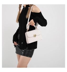 Detail of white quilted crossbody bag featuring a gold heart-shaped metal twist lock