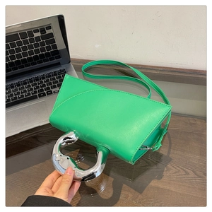 Detail of green leather handbag with oversized silver circular handle on wooden table