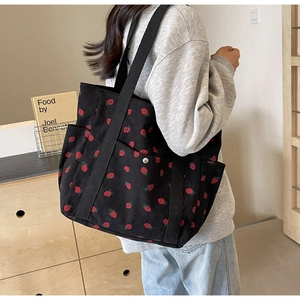 Close-up of black corduroy tote bag with strawberry embroidery and metal button detail