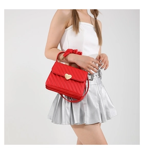 Detail of red quilted handbag featuring a heart-shaped gold buckle and ruched fabric handle