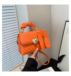 Detail of orange quilted crossbody bag featuring heart clasp and mini pouch attachment