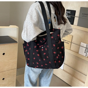 Détail du sac cabas en velours côtelé noir avec broderie fraise et bandoulière large