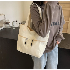 Detail of beige canvas tote bag with functional black zipper pockets on a wide shoulder strap
