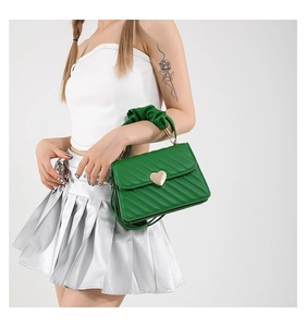 Close-up of green quilted shoulder bag with golden heart lock and ruched handle