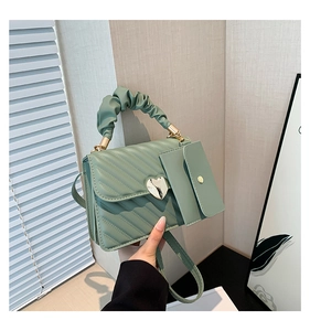 Detail of green quilted crossbody bag with cloud handle and heart-shaped metal buckle