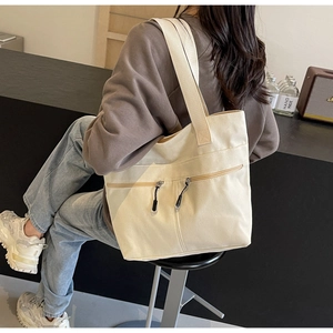 Detail of off-white canvas tote bag with dual front zipper pockets and wide shoulder straps