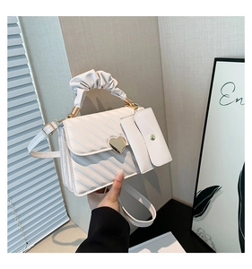 Close-up of white quilted handbag with heart-shaped buckle and ruffled handle