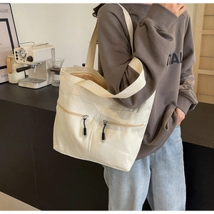 Detail of off-white canvas tote bag featuring dual front zipper pockets for daily commute
