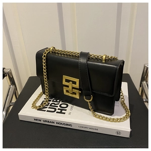 Detail of black leather shoulder bag with gold geometric lock and chain strap on books