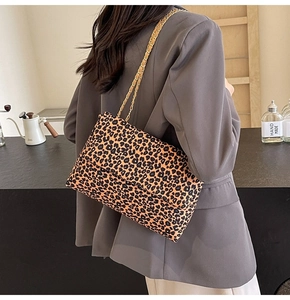 Detail view of leopard print tote bag with gold chain strap worn by a model in a cafe