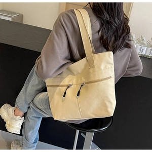 Detail of beige canvas tote bag showing double front zipper pockets and shoulder straps