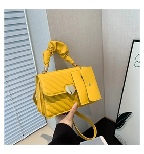 Detail of yellow quilted handbag with heart buckle and pleated handle held by hand