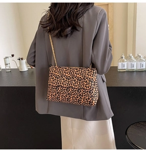 Model wearing leopard print chain shoulder bag with gold hardware in a chic cafe setting