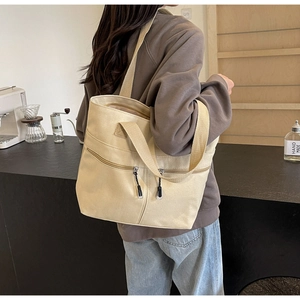 Detailed view of beige canvas tote bag with functional double zipper front pockets