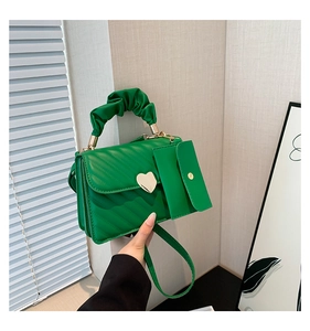 Detail of vibrant green square handbag featuring pleated handle and gold heart clasp
