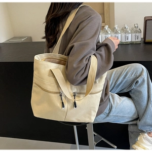 Detail of beige canvas tote bag showing front zipper pockets and multiple carry straps