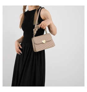 Detail of beige quilted handbag with gold heart buckle and ruffled handle on black dress