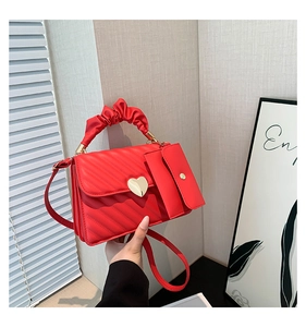 Detail of red quilted crossbody bag with heart buckle and pleated handle