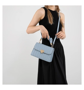 Detail of light blue quilted crossbody bag with heart buckle and pleated handle
