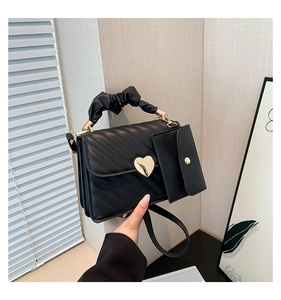 Close-up of black quilted handbag featuring a golden heart lock and pleated handle