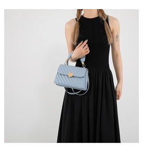 Detail of light blue quilted crossbody bag with golden heart lock worn by model