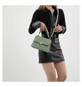 Detail of green quilted handbag with gold heart buckle and ruffled handle on model