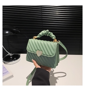 Detail of light green quilted handbag featuring a gold heart clasp and cloud handle