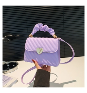 Detail of lavender quilted mini bag with heart lock and pleated handle on a desk