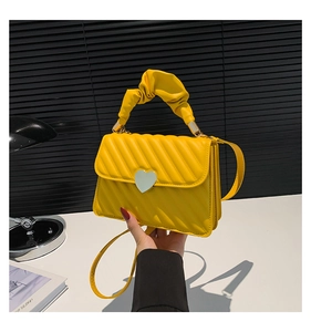 Detail of yellow quilted crossbody bag with heart clasp and ruffled handle grip