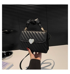 Close-up of black quilted handbag featuring a silver heart-shaped clasp and pleated handle