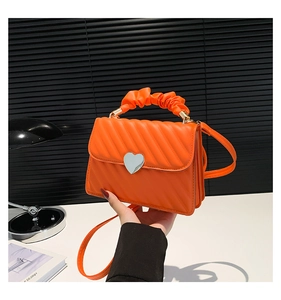 Detail of orange quilted leather handbag with heart lock and ruched cloud handle