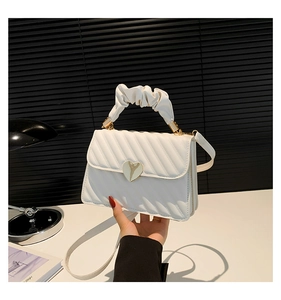 Detail of white quilted handbag with a gold heart clasp and pleated cloud handle