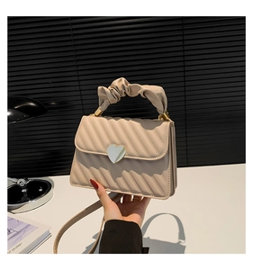 Detail of beige quilted crossbody bag featuring a heart-shaped metal twist lock and ruched handle