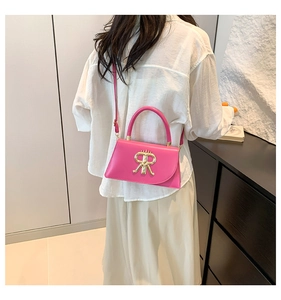 Detail of rose pink crossbody bag with gold letter R clasp shown on a shoulder