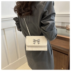 Detail of white chain shoulder bag with a silver bow clasp worn by a model