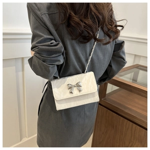 Detail of white glossy leather shoulder bag with silver metal bow and chain strap