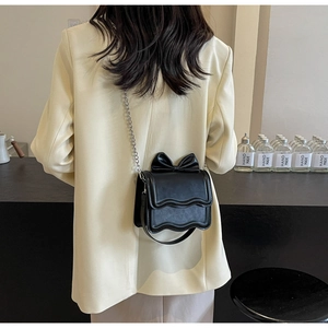 Detailed view of a black crossbody bag with bow decoration and silver chain on model