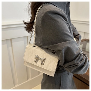 Detail of white crinkled leather crossbody bag with silver bow buckle worn by model