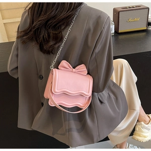 Pink square crossbody bag with bow detail and silver chain strap shown on a model
