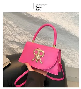 Close-up of rose red leather square bag featuring a large gold metal R-shaped buckle