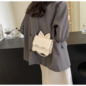 Detail view of cream mini crossbody bag with bow decoration and wavy flap edge