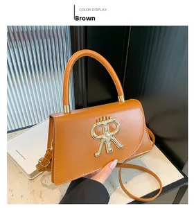 Detail of a brown leather crossbody bag featuring a large gold R metal buckle and handle