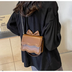 Detail of a brown crossbody bag featuring a 3D bow and unique wavy stitched edges