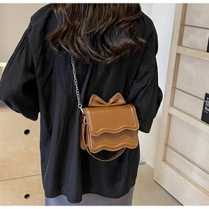 Detailed view of brown crossbody bag with wave edges and large bow on a model