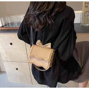 Detail of light khaki crossbody bag with wave flap and decorative bow accent